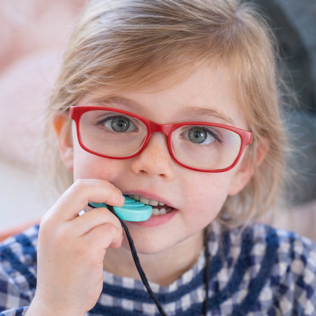 Child wearing red glasses chewing on a turquoise TalkTools Chewy Necklace pendant, designed for safe oral sensory support.